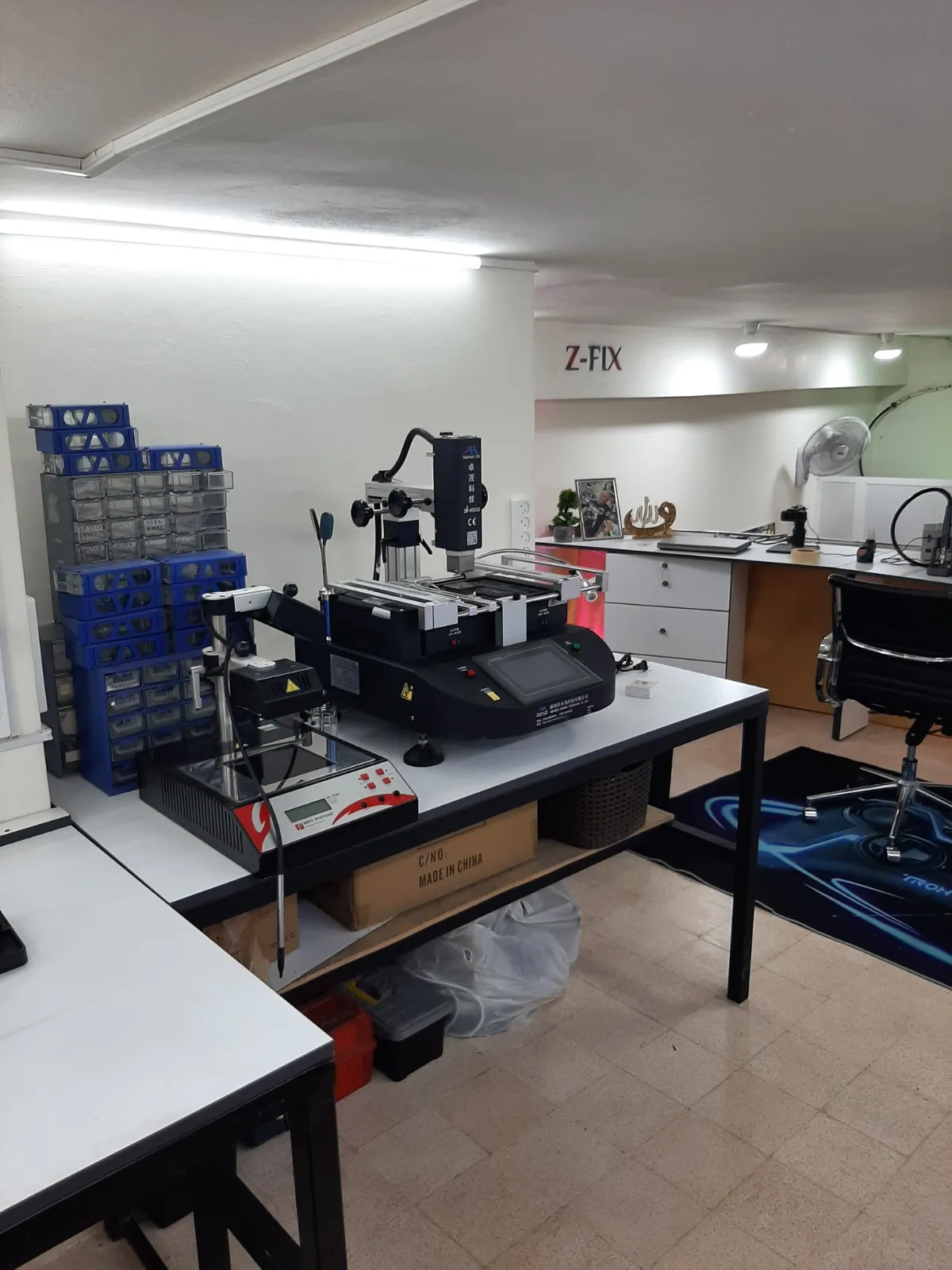 The Z-Fix repair laboratory in Tripoli: a professional BGA rework station on the workbench, component storage drawers and surrounding workstations, with the Z-Fix name on the wall